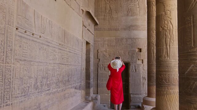 A woman in a red dress exploring the ruins of the Philae Temple, Aswan, Egypt.