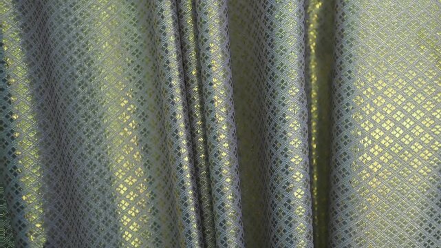 Curtains featuring an intricate diamond pattern known as lai khao lam tad combine geometric shapes with shimmering gold threads.