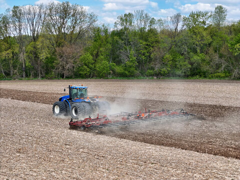 Blue tractor pulling a red field cultivator to prep the field for spring planting.