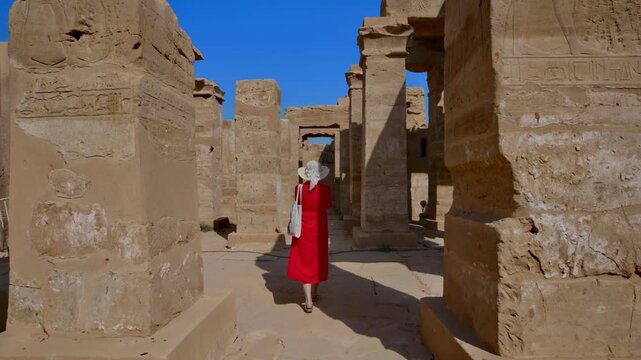 A woman in a red dress exploring the ruins of the Karnak Temple, Luxor, Egypt.