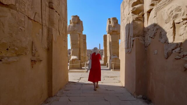 A woman in a red dress exploring the ruins of the Karnak Temple, Luxor, Egypt.