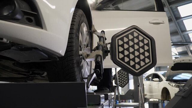 Diagnostics and balancing of wheels at a close-up view in a modern service station. The car moves slowly while wheel balancing equipment is used.