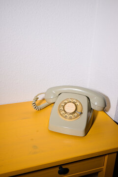 Close-up of an old rotary dial telephone on a yellow wooden table.
