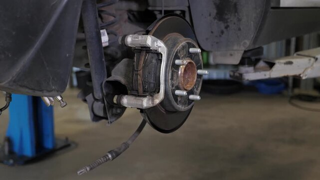 A detailed view of a dismantled wheel with a brake pad and shock absorbers in a vehicle at a repair facility, a vehicle undergoing maintenance on a lift in a car repair shop.