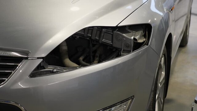 A detailed view of a vehicle without a functioning headlight at a repair facility, where a malfunctioning headlight is being replaced in a contemporary auto repair shop.