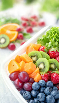 A colorful assortment of fresh fruit arranged in a bowl, including strawberries, kiwi, grapes, blueberries and melon beside green lettuce. Bright natural lighting and shallow depth of field.