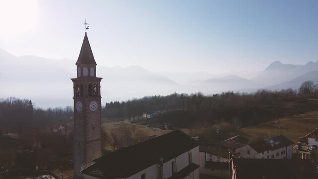 Horizontal 2.7K 24fps aerial drone video rising vertically over a concrete bridge spanning a turquoise river valley in the mountain village of Lauco, Friuli, Italy, during a cold winter day