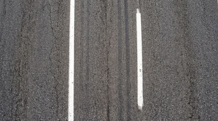 Fototapeta premium Overhead view of worn highway asphalt with white lane lines and weathered textures
