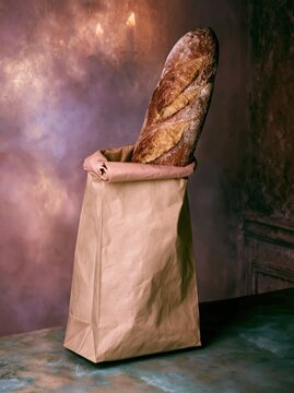 Brown paper bag containing a fresh crusty baguette on a textured surface in a moody interior for artisan bakery branding, food delivery and gourmet packaging mockup