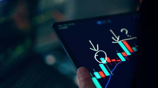 Financial analyst using graphic tablet examining stock market candlestick charts screen. Professional investor utilizes a stylus pen on a digital tablet to analyze currency trends