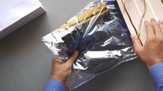 Person unpacking small blue and yellow clothing items from plastic delivery bags on gray surface