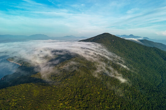 Clouds drift over the lush green jungle landscape of Son Tra Peninsula in Danang Vietnam where the mountains meet the blue ocean during a bright morning