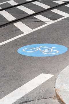 A blue bicycle lane symbol sits on the pavement beside a crossing, where road marking clarifies cycling movement and urban safety at the curb