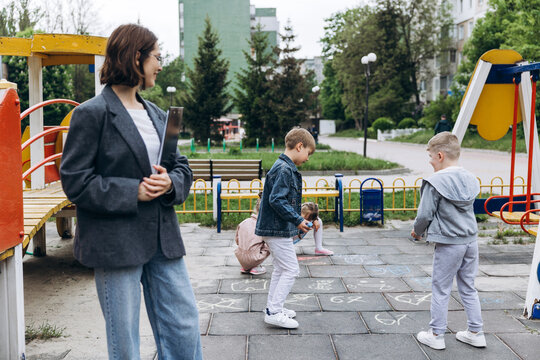 Smiling positive teacher supervising children playing in urban playground outdoor