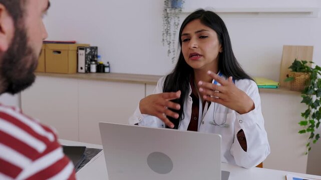 Indian female doctor listening carefully to a male patient's health concerns during a medical consultation in her office, providing professional advice and showing empathy at the clinic