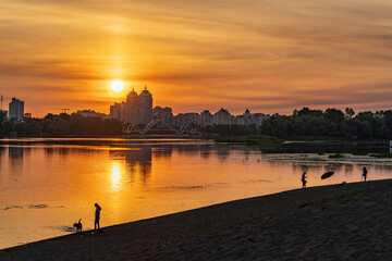 Naklejka premium Beautiful golden sunset over Dnieper river with people silhouettes on the beach and Kyiv city skyline