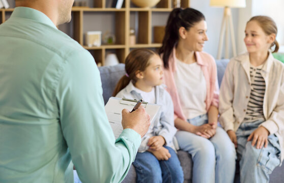 Family therapist counsels mother and daughters in session. A psychologist with clipboard guides children toward communication and therapy at home. Clear concept of counseling support.