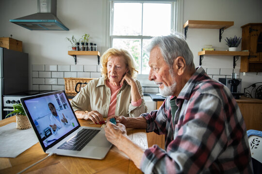 Senior couple consulting doctor online at home kitchen