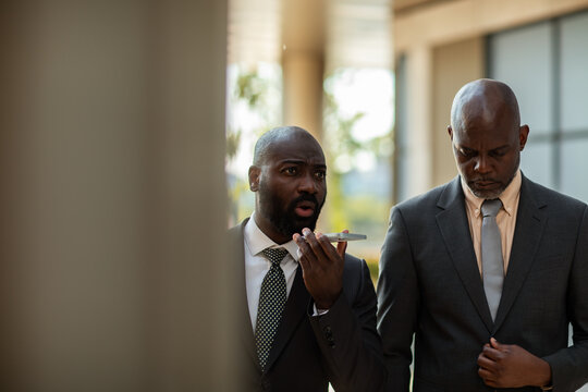 Two businessmen using smartphone voice assistant outside office