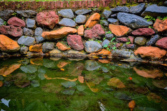 Natural stone retaining wall reflecting in clear pond water with mossy rocks and vibrant earthy colors outdoors