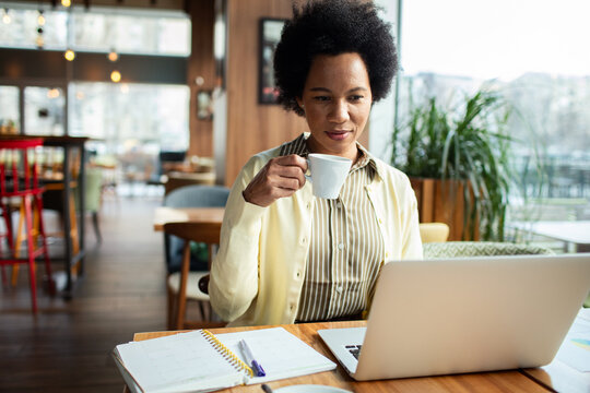 Woman drinking coffee while working on laptop in cafe