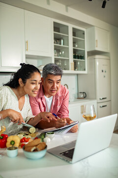 Man and woman cooking together with laptop in home kitchen
