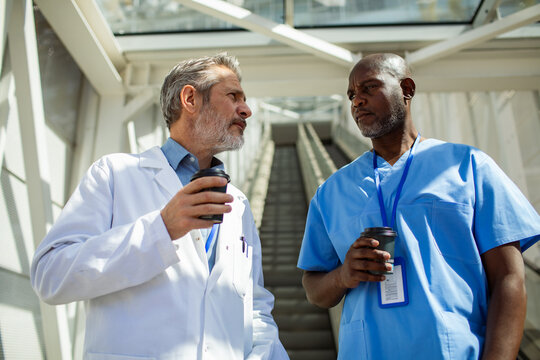 Two medical colleagues talking during coffee break in hospital corridor
