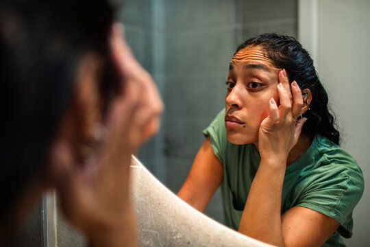 Woman examining eye area in bathroom mirror