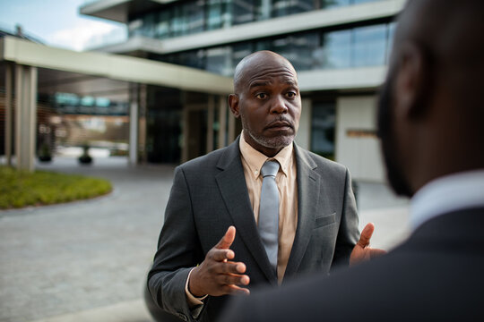 Businessman gesturing during conversation outside modern office