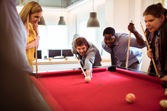 Coworkers playing pool in modern office break room