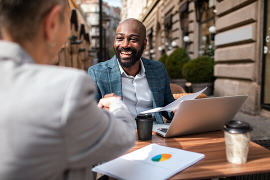 Smiling professionals shaking hands during outdoor business meeting at city cafe