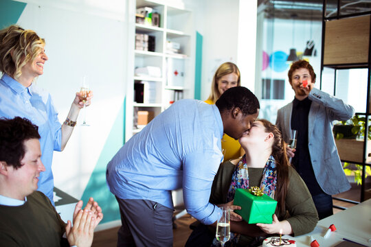Coworkers celebrate office birthday with gift and kiss
