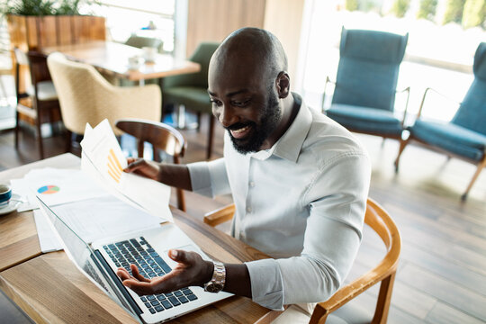 Happy businessman analyzing charts on laptop in cafe