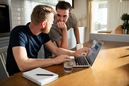Two men collaborating on laptop at home kitchen table