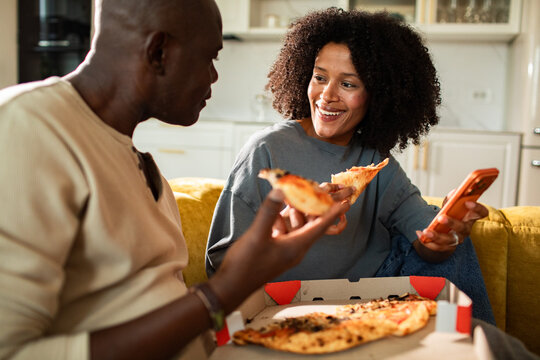 Smiling couple sharing pizza on couch at home