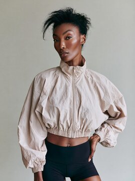 Woman of African descent wearing a camel cropped windbreaker jacket poses confidently against a neutral background, showcasing modern fashion and style