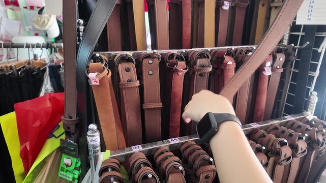 Close up of customer hand choosing brown leather belt from a display rack in shop, Hand selecting casual brown leather belt hanging on hanger in clothing store.