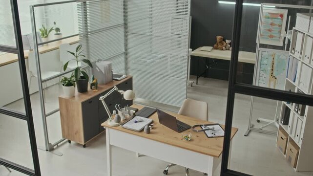 High angle shot of empty pediatric clinic office showing desk with laptop, stethoscope, and examination table with teddy bear. For healthcare marketing and medical services advertising