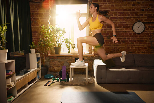 Woman performing high knee jump during intense home workout. Concept of explosive training, cardiovascular endurance, athletic conditioning and high intensity exercise.