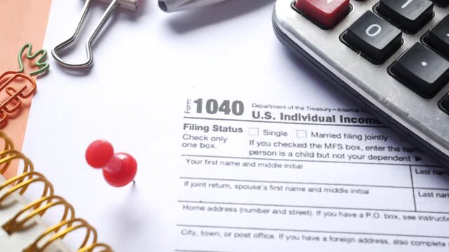 Close-up view of us individual income tax form 1040 on a white desk with calculator, paper clips, and note pad, rotating shot