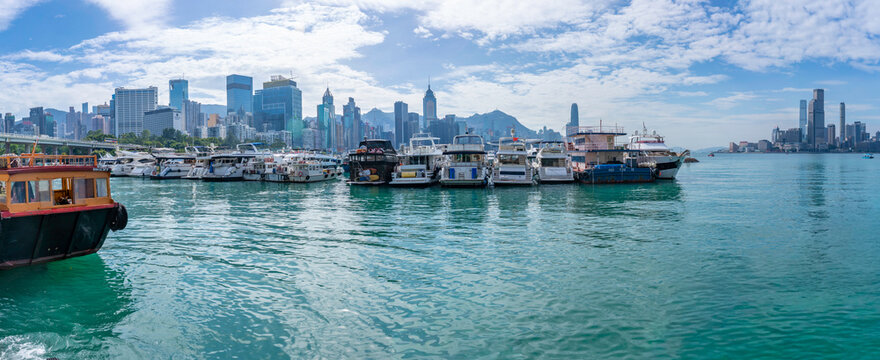 View of Hong Kong skyline and Victoria Harbour from Hong Kong Island on a sunny day with boats in the foreground