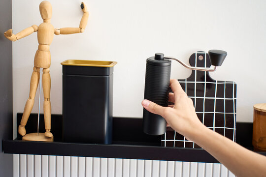Hand picks up manual coffee grinder stored on kitchen shelf for coffee preparation