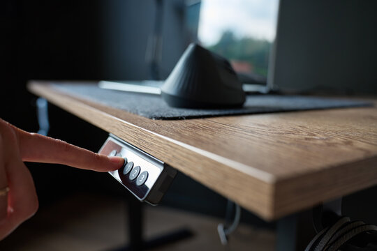 Close up of finger pressing control button on electric adjustable desk with wooden surface