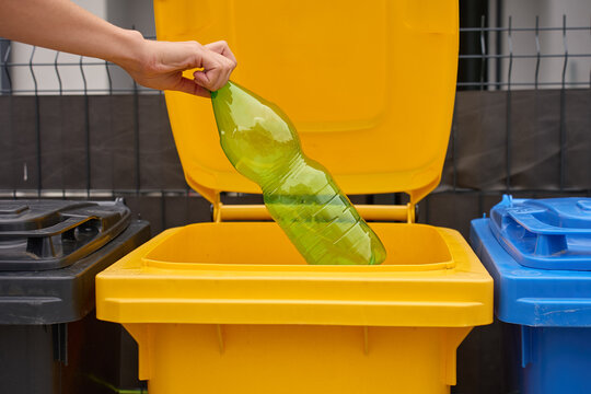 Hand places empty plastic bottle into yellow recycling bin for waste sorting