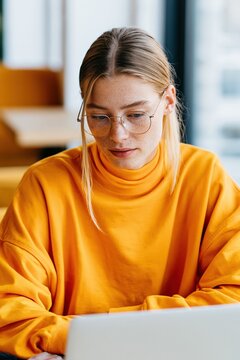 Young woman in bright orange turtleneck using laptop for website banner and social media profile background
