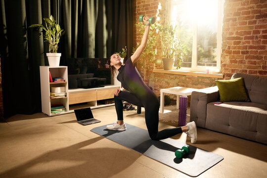Woman performing weighted yoga twist lunge with dumbbell during home mobility workout. Concept of flexibility, balance, functional strength, home fitness and mindful wellness.