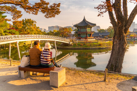 Hyangwonjeong Pavilion stands near a calm lake as visitors enjoy autumn in Gyeongbokgung Palace during golden hour in Seoul, South Korea