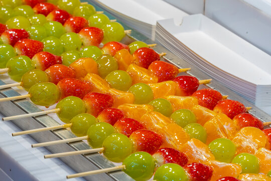 Colorful fruit sticks displayed on a market stall in a busy shopping area at night in Seoul, South Korea