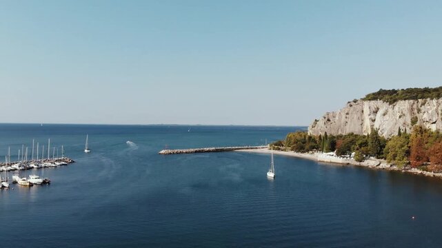 Horizontal 2.7K 60fps drone video flying forward over the blue water of Sistiana Bay, Italy, showing moored boats and white rocky cliffs