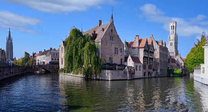 View of Bruges with the Belfry, Dijver canal, and Church of Our Lady surrounded by historic buildings and trees in Flanders, Belgium
